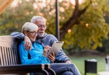 Older couple sitting on bench using tablet outdoors
