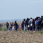 Group walking through a barren field carrying bags