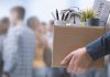 Person holding box with office items and newspaper