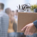 Person holding box with office items and newspaper