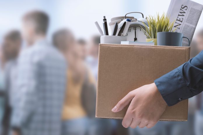 shutterstock_2157465795.jpg featured image Person holding box with office items and newspaper