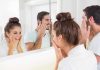 A couple smiling at their reflections in a bathroom mirror while applying skincare products