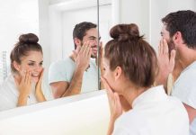 A couple smiling at their reflections in a bathroom mirror while applying skincare products