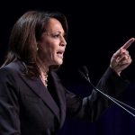 Person speaking at podium with raised finger