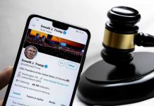 Smartphone displaying Twitter profile near a judge's gavel.