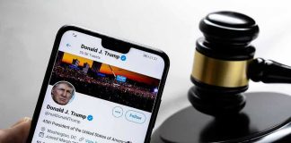 Smartphone displaying Twitter profile near a judge's gavel.