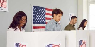 People voting in booths with American flag backdrop.