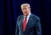 Dem States SUE Trump – Government EXPLODES! Man in suit with red tie speaking on stage.