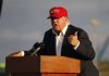 Trump’s Secretive Air Base Talks—What’s Brewing? Person speaking at a podium wearing a red hat.