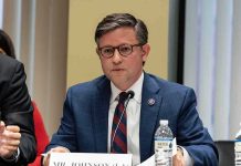A public official speaking at a meeting with a nameplate in front of him