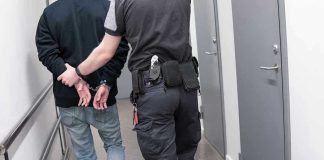 Officer escorting handcuffed person down hallway.