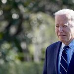 Man in a suit standing outdoors, blurry background.