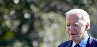 Man in a suit standing outdoors, blurry background.