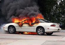 A white car engulfed in flames with thick black smoke rising
