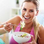 Woman smiling and eating a salad bowl.