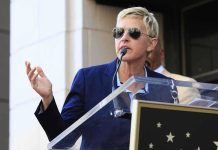 Ellen DeGeneres FLEES Britain – Comes RUNNING Home A woman in sunglasses speaking at a podium during an outdoor event