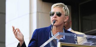 Ellen DeGeneres FLEES Britain – Comes RUNNING Home A woman in sunglasses speaking at a podium during an outdoor event