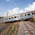 An overturned train on a railway track surrounded by vegetation