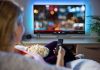 Netflix ACQUIRES Competitor For $72 Billion – Stuns Industry Person sitting on a couch watching a movie on a TV with popcorn in hand