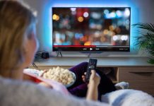 Netflix ACQUIRES Competitor For $72 Billion – Stuns Industry Person sitting on a couch watching a movie on a TV with popcorn in hand