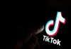 Finger pointing at TikTok logo on a screen.