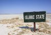 A weathered sign reading 'ISLAMIC STATE' in a barren landscape