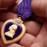 National Guard Troops SHOT in DC Receive RARE Recognition A hand holding a Purple Heart medal with a purple ribbon