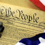Close-up of the U.S. Constitution with a firearm and American flag