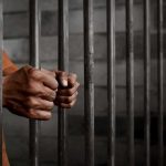 Hands gripping prison cell bars.