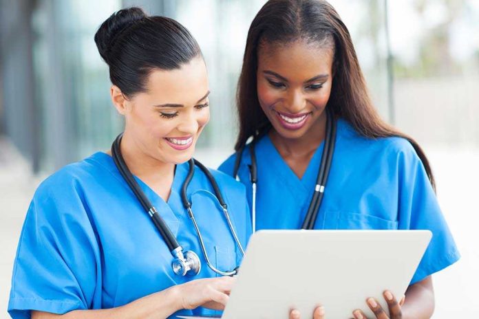 shutterstock_158379851 Two nurses in blue scrubs smiling while looking at a tablet