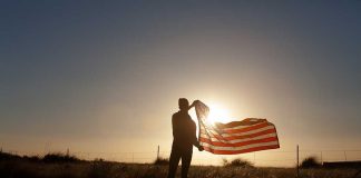 Silhouette of a person holding an American flag against a sunset