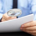 A person using a magnifying glass to examine a document closely