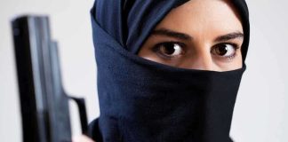 A woman in a black hijab holding a gun with an intense gaze