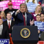 Person speaking at rally with crowd behind podium