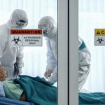 Healthcare workers in protective gear in quarantine room.