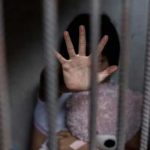 Kids Seized — Caller Vanishes Child behind bars, hand raised, holding a teddy bear.