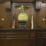 Court Backs Teen’s Conversion Claim Judges bench in an empty courtroom, scales emblem above.