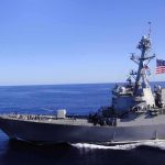 Naval destroyer sailing on open sea with flag flying