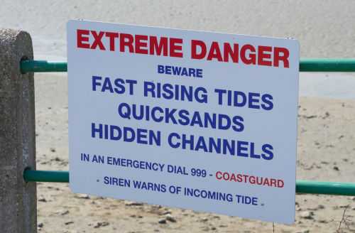 shutterstock_1493096012 Sign warning of tides, quicksand, hidden channels.