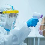 Contact Tracing Collapses—Virus Accelerates Healthcare worker in PPE checks patient temperature with infrared thermometer