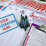 Voter registration table with forms, pens, and informational materials