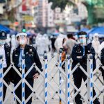 Crowded Feast Turns Killing Ground Police officers in masks stand behind portable barricades on a city street
