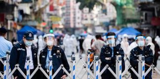 Police officers in masks stand behind portable barricades on a city street