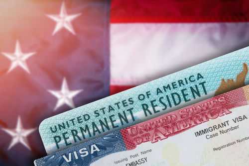 shutterstock_1981089794 Green card and visa with U.S. flag background.