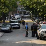 Police officers secure a residential street with patrol cars and yellow tape