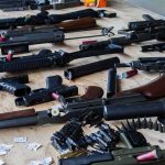 Assorted firearms and ammunition laid out on a wooden table