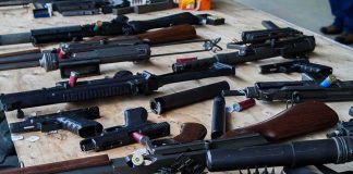 Assorted firearms and ammunition laid out on a wooden table