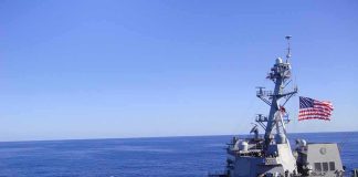 Naval destroyer sailing on open sea with flag flying