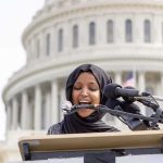Woman in hijab speaking at podium with microphones