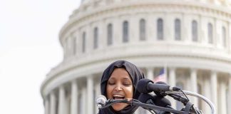 Woman in hijab speaking at podium with microphones